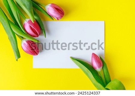 Bouquet of pink tulips and greeting card on yellow background. Invitation to holiday.