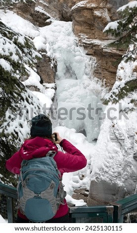 Tourist takes Pictures of Johnston Canyon Waterfall - Frozen Lower Falls with turquoise pool below Banff National Park AlbertaCanada 