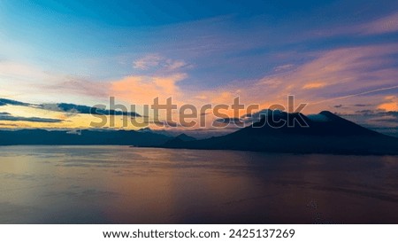 Vibrant hues of morning grace the skies above Lake Atitlán, reflecting off the calm lake in a stunning display.