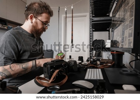 An adult man is deeply focused on his photography equipment at a well-organized workspace, surrounded by the tools of his creative profession