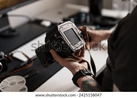 An adult man is engrossed in adjusting the settings on a medium format camera, highlighting meticulous attention to detail in a professional studio