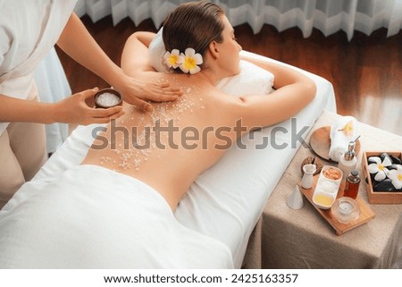 Woman customer having exfoliation treatment in luxury spa salon with warmth candle light ambient. Salt scrub beauty treatment in health spa body scrub. Quiescent Royalty-Free Stock Photo #2425163357