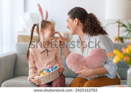 Happy holiday! Mother and her daughter with painting eggs. Family celebrating Easter. Cute little child girl is wearing bunny ears.