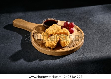 Crispy fried cheese with grapes and berry jam on a rustic wooden serving board.