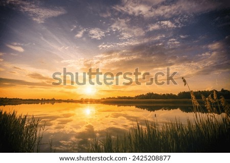 Sunset or sunrise above the pond or lake at spring or early summer evening or morning with cloudy sky background and reed grass. Springtime landscape. Water reflection. Vintage film aesthetic.