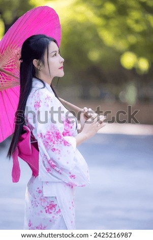 Asian woman wearing japanese traditional kimono. Beautiful Woman smiling, holding a umbrella walking outside. Woman in Kimono dress enjoying and walking on street outdoors in slow motion.