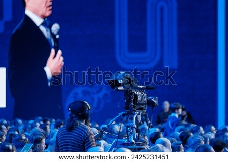 A speaker delivers a speech to a captivated audience at a professional conference, captured on camera.