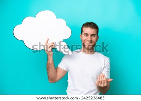 Young caucasian man isolated on blue background holding a thinking speech bubble and doing coming gesture