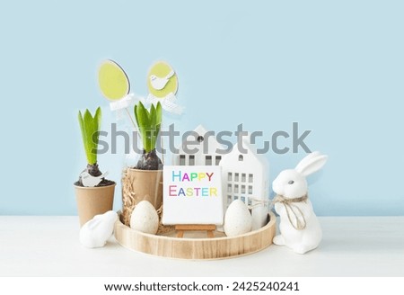 Delicate beautiful festive Easter composition on a light blue background.  Spring flowers, white rabbit, Easter eggs symbol of the holiday.  Happy Easter holiday concept.  Front view.