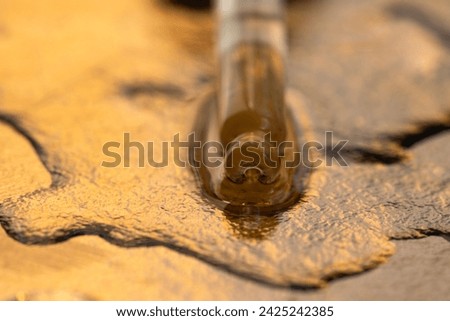 A glass dropper with a cosmetic emulsion lies in the liquid, close-up, yellow background.