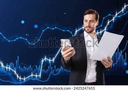 Attractive young european business man talking on the phone and holding document with glowing and growing business chart on blurry blue background. Financial growth, trade and stock concept