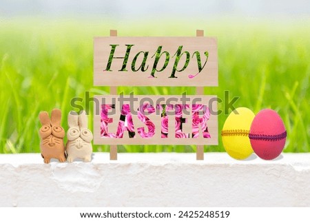 Happy Easter sign with flower and green leaves pattern on cement wall with clay rabbit and easter eggs over blurred green grass background, Easter card background idea