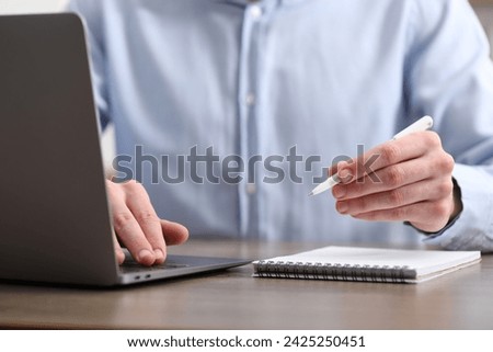 E-learning. Man taking notes during online lesson at table indoors, closeup