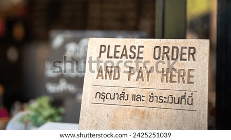 "Order and pay here" wooden banner (in English and Thai langauge) that placed on the counter of cafe and restaurant. Sign for business place object photo. Close-up.