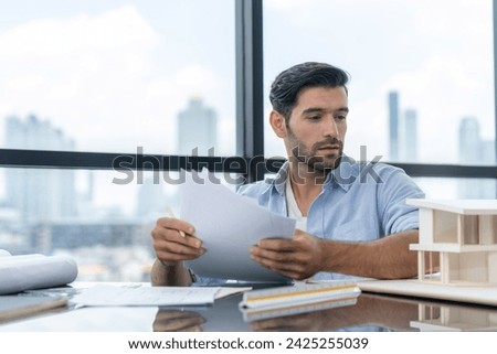 Skilled caucasian architect engineer holding blueprint on desk in modern office. Smart interior designer compared between blueprint and house model. Project, blueprint, construction, project. Tracery.