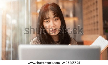 A beautiful Asian woman is working remotely at a cafe co-working space, focusing on her laptop computer. people and modern life concepts