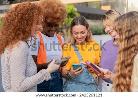 Group of multiracial young woman looking their smartphones and using them. Friends texting and sharing social media content with the mobile phones smiling and enjoying outside