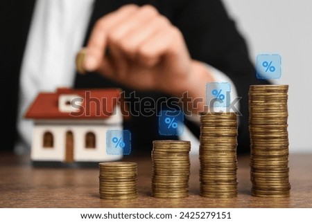 Mortgage rate. Woman putting coin into house shaped money box, closeup. Stacked coins and percent signs