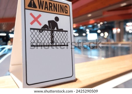 Close-up image a white warning don't climb over the fence signage is displayed on glass barrier in departments store.
