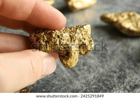Woman holding gold nugget at grey textured table, closeup. Space for text