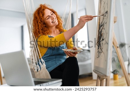 Happy and relaxed young woman enjoying her free time at home, expressing her creativity and painting a new picture.