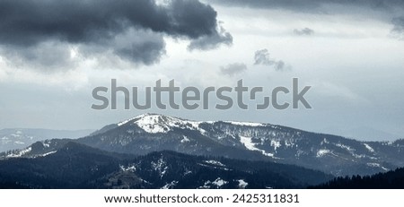 Dramatic dark gray clouds over the Vysoky Verkh mountain in the Ukrainian Carpathians. Panoramic view. Background with winter mountain landscape in February messenger. Real photo, not fake, not AI