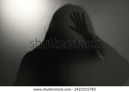 Silhouette of ghost behind glass against light grey background
