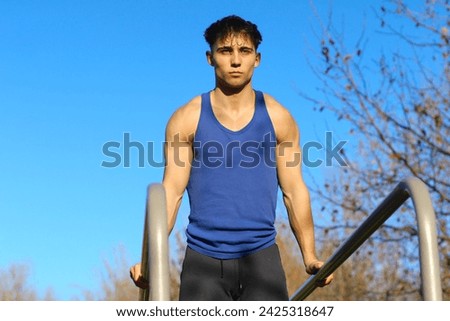 Caucasian young man exercising on bars with a determined look, dressed in sportswear, outdoors. Muscle training concept