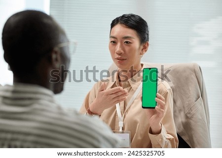Smiling bank manager showing client smartphone with green screen, explaining how to use banking app