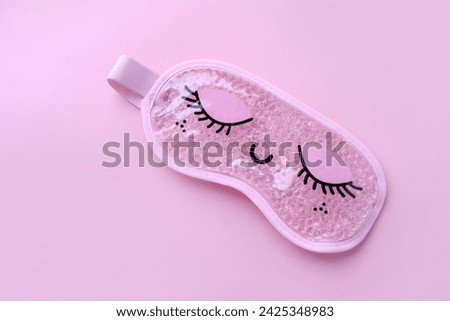 Pink sleep mask with closed eyes on it on pink background. Top view, flat layer. The concept of vivid healthy dreams.