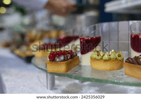 Variety of sweet and savory canapes and desserts displayed on glass shelf. Canapes topped with ingredients like caviar, salmon, and vegetables. Desserts include tarts, cakes, and pastries. Royalty-Free Stock Photo #2425356029