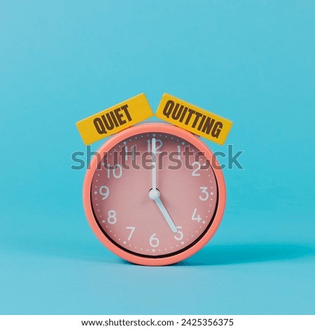the text quiet quitting written on two yellow rectangular pieces, on a pink clock striking five, on a blue background Royalty-Free Stock Photo #2425356375