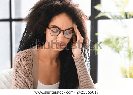 Sad overworked fatigued exhausted tired young african businesswoman freelancer rubbing her temples, having headache migraine, thinking about problems, issues, resignation, aborting, painful memories Royalty-Free Stock Photo #2425365017