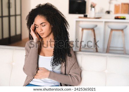 Young african woman having stomach ache, period crumps, feeling sad and depressed, suffering from headache migraine, indigestion, having bad health medical condition Royalty-Free Stock Photo #2425365021