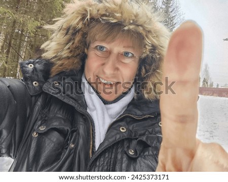 Happy, cheerful middle-aged woman in a warm jacket and a hood with fur taking selfie in winter outdoors. Female Traveler in Alaska, Lapland, Arctic, Siberia Royalty-Free Stock Photo #2425373171