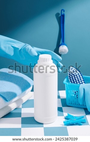 A hand with rubber gloves is preparing to pick up a white bottle of detergent without a label. Cleaning products placed on a blue and white checkered background. Creative ideas for advertising