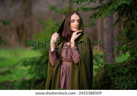 Portrait of Amazing fairytale princess in elven green cape and vintage dress standing in winter forest. Warm art work with queen elegant vintage lady.