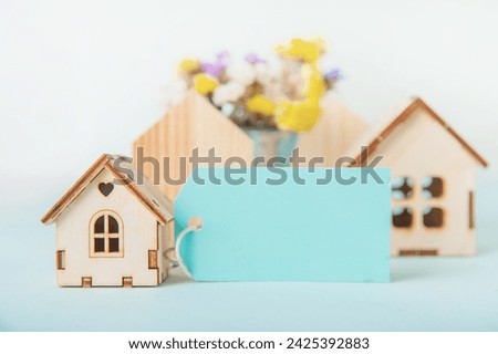 Happy Easter greeting card. Miniature wooden house. Rabbits, colorful eggs, spring flowers with tag for text.