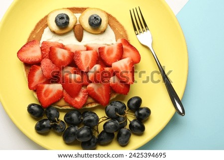 Creative serving for kids. Plate with cute owl made of pancakes, berries, cream, banana and almond on color background, top view
