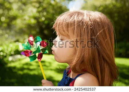 Young girl, outdoor and blowing pinwheel, garden and enjoying freedom of outside and happy. Pretty little child, backyard and summer for playing, toy and windmill for school holidays and happiness Royalty-Free Stock Photo #2425402537