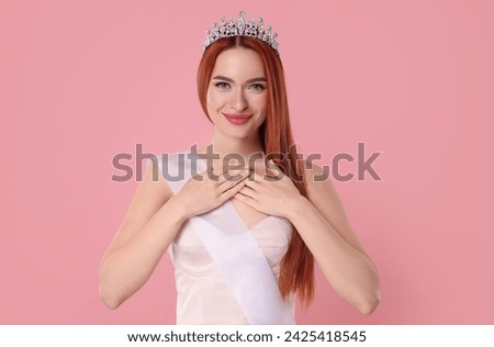 Beautiful young woman with tiara and ribbon on pink background