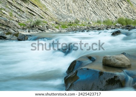Beautiful flowing water in mountainous place, long exposure of fast strong stream. River in the mountains, rocky hill on the background