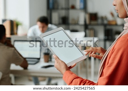Tablet with blank screen in hands of young Muslim female manager standing in front of camera in coworking space