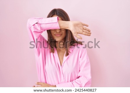 Young hispanic woman wearing glasses standing over pink background covering eyes with arm, looking serious and sad. sightless, hiding and rejection concept  Royalty-Free Stock Photo #2425440827
