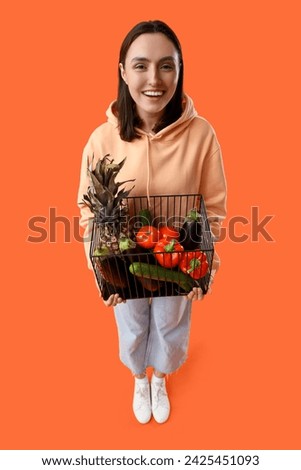 Young woman with basket of healthy food on orange background