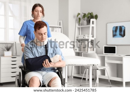 Injured young man after accident in wheelchair with doctor at hospital Royalty-Free Stock Photo #2425451785