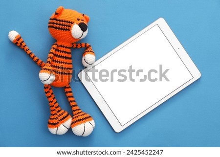 Modern tablet and toy tiger on blue background, flat lay. Space for text