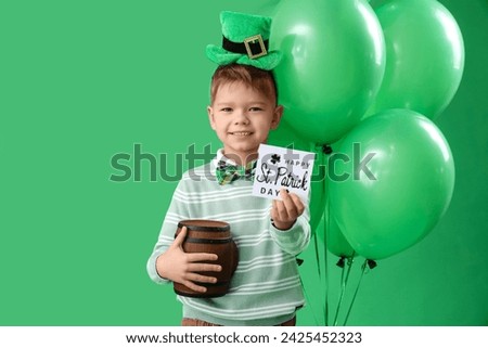Cute little boy with leprechaun's hat, balloons and greeting card for St. Patrick's Day celebration on green background