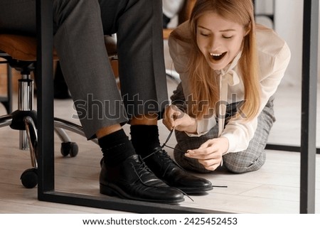 Young woman tying her colleague's shoe laces in office. April Fools' Day celebration Royalty-Free Stock Photo #2425452453