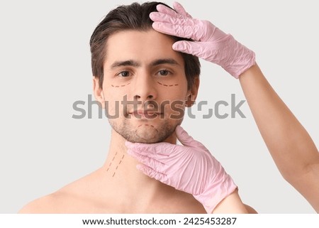 Plastic surgeon and young man with marked face on light background, closeup